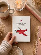 Hand holding a card with red chilies and text on a wooden table with a cup of coffee and candle.