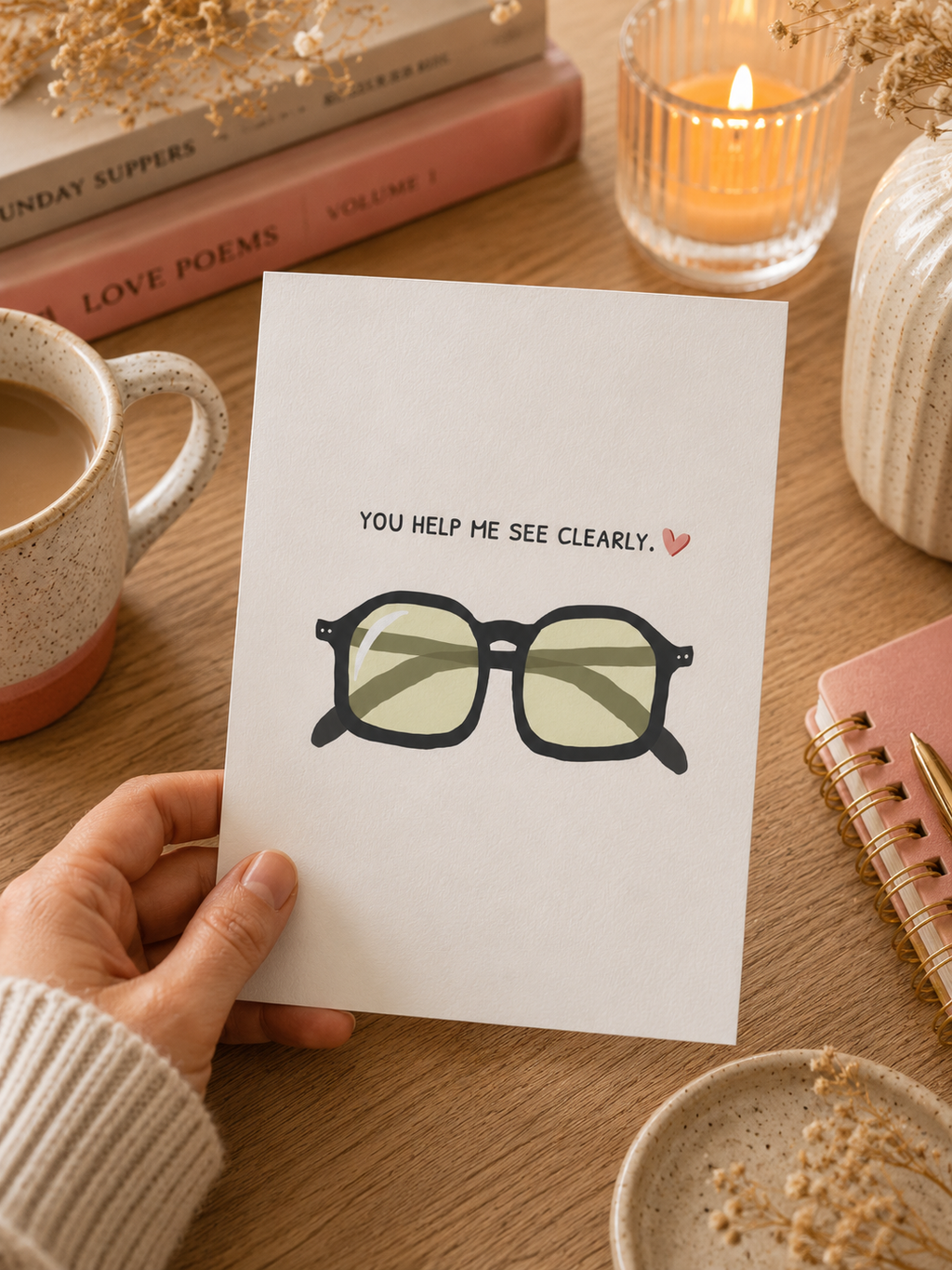 Hand holding a card with glasses illustration and text on a cozy table setting.