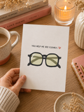 Hand holding a card with glasses illustration and text on a cozy table setting.