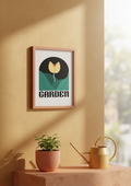 Framed artwork with a tulip design and 'Garden' text on a beige wall with a plant and watering can.